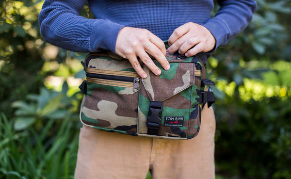 Person wearing the LGD as a hip pack. It's positioned at the front of their body, and they are zipping open the main compartment.